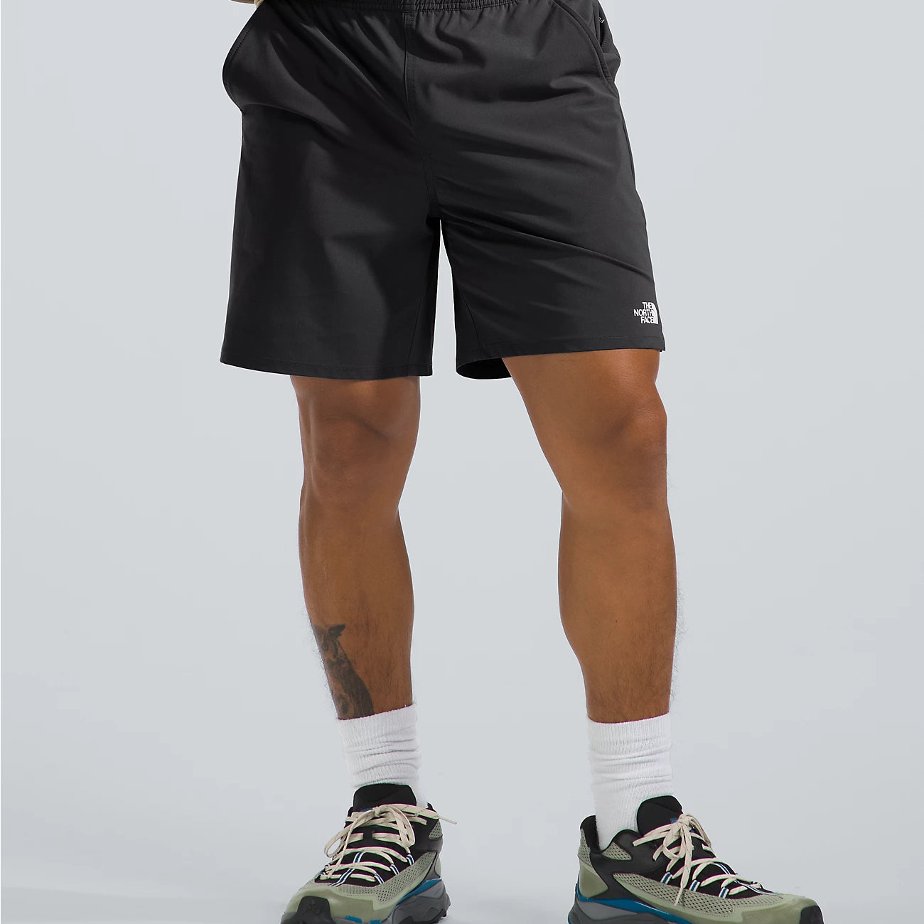 Person wearing black shorts with a brand logo on a light gray background