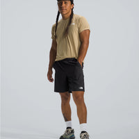 Person wearing a beige t-shirt, black shorts, and a cap on a light gray background