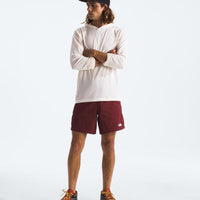 Person wearing a white long-sleeve shirt, maroon shorts, and a black cap on a light gray background