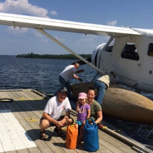 Family with luggage on a dock next to a small airplane over water