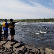 Group of people standing on a rocky riverbank pointing at the water