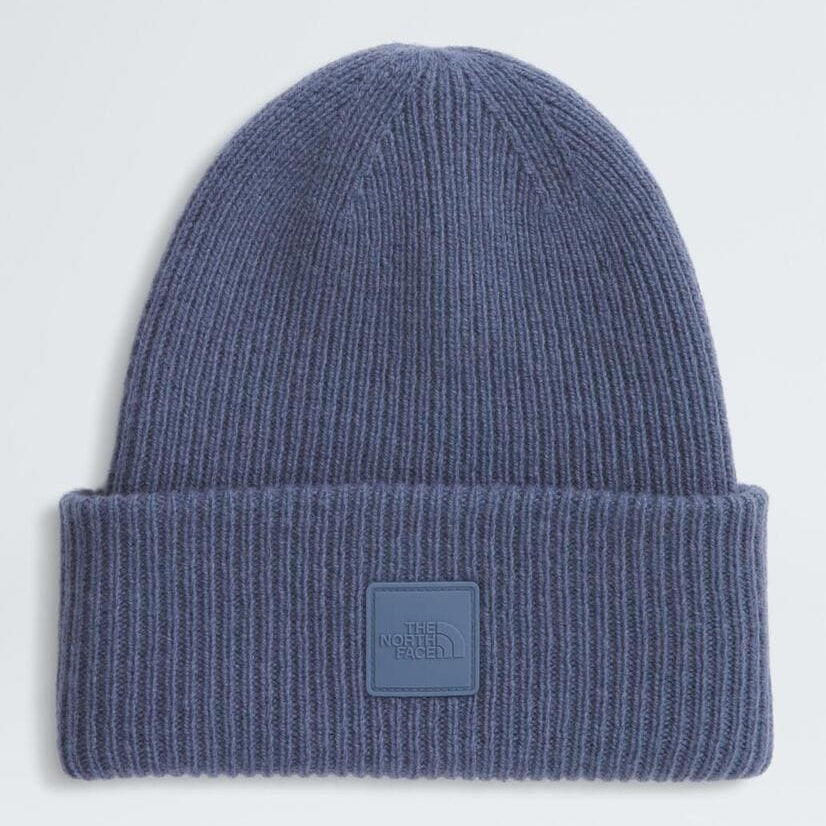 Blue knit beanie with a logo patch on a light gray background
