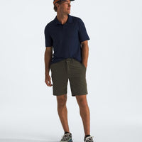 Man wearing a navy polo shirt, green shorts, and a cap on a white background