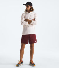 Person wearing a white long-sleeve shirt, maroon shorts, and a black cap on a light gray background