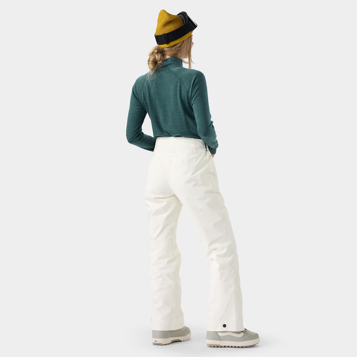 Person wearing a green jacket, white pants, and a yellow and black beanie on a white background