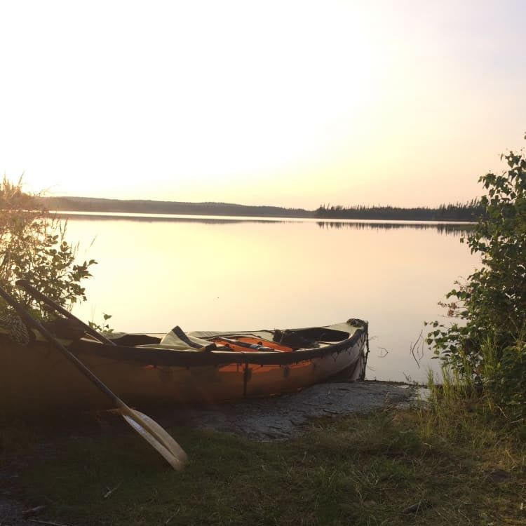 Canoe on a grassy bank by a lake at sunset